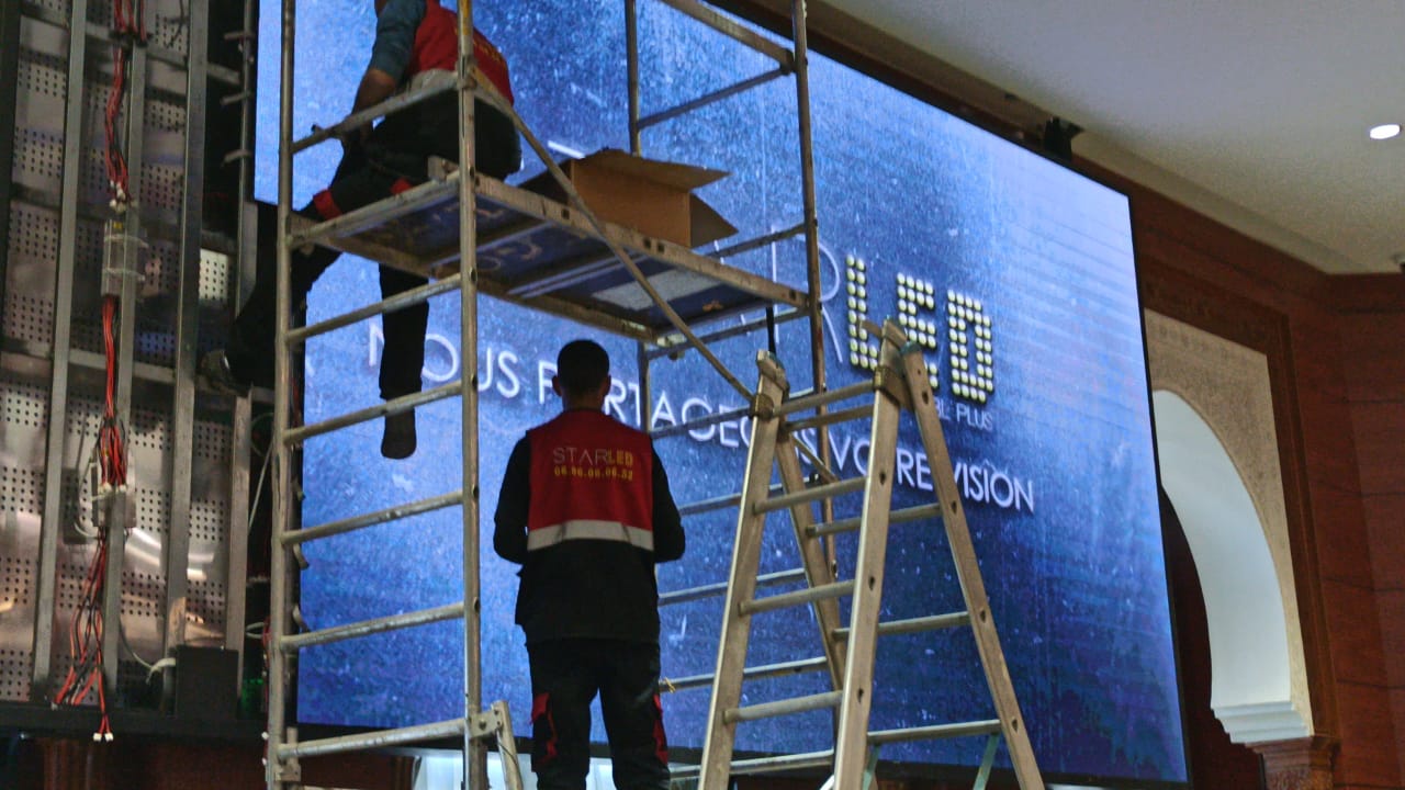 Techniciens réglant un écran LED monté sur échafaudage dans une salle à décor traditionnel